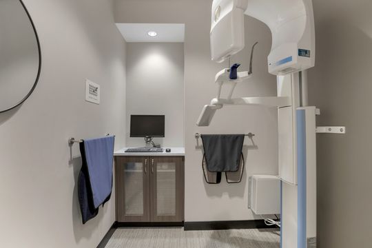This image of the dental imaging alcove at Soult and Swanson Family Dentistry shows panoramic imaging equipment, small cabinet, wall monitor, and clean clinical wall finishes.