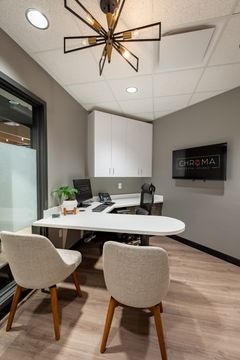 This image of the private consultation room at Chroma Dental Studio shows a compact meeting table, modern chandelier, wall monitor, gray cabinetry, and wood flooring.