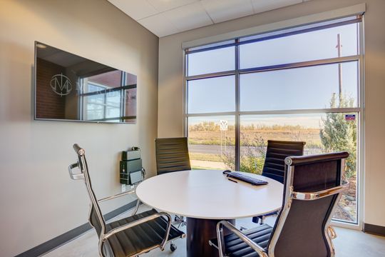 This image of the consultation room with view at Meridian Periodontics of Central Park shows a round table, purple chairs, wall monitor, large windows, and landscape views.