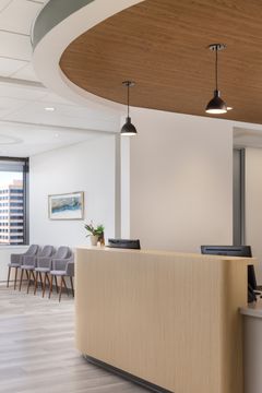 This image of the reception counter detail at Core Dermatology shows a rounded wood counter, pendant lights, curved wood ceiling feature, and patient seating beyond.