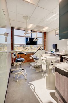 This image of the compact operatory view at Meridian Periodontics of Central Park shows a dental chair, wall monitor, windows, round work counter, and clinical equipment.