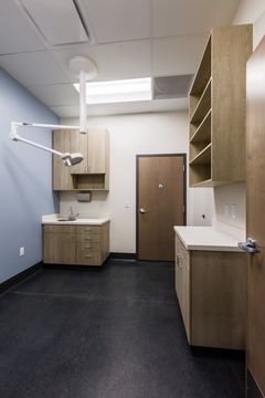 This image of the exam room sink area at Montclair Animal Clinic shows a sink cabinet, wall cabinetry, exam room door, dark flooring, and clean veterinary clinic finishes.