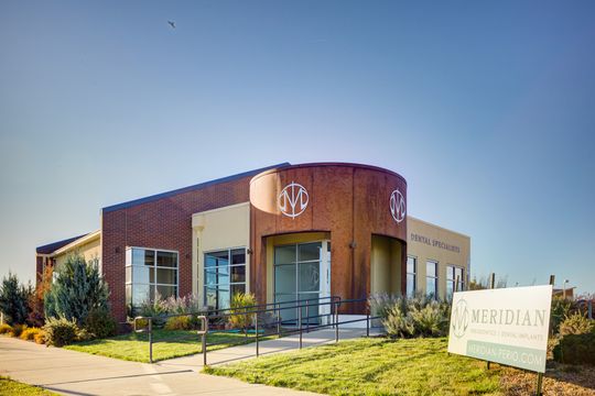 This image of the exterior entry and monument sign at Meridian Periodontics of Central Park shows the front entrance, curved wood facade, sidewalk landscaping, and roadside monument sign.