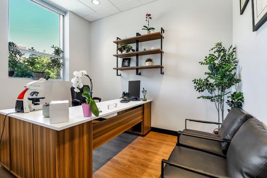 A welcoming office and consultation space at Elevation Dermatology with wood desk, leather seating, wall shelving, and plant decor.