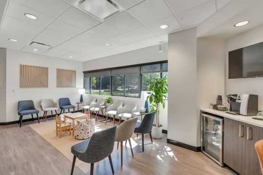 A bright and welcoming waiting area at Foundations Orthodontics with comfortable seating, children’s furniture, geometric wood wall art, plants, and a refreshment station.