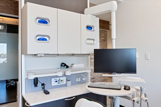 A detailed view of a clinical workstation at Arvada Dental Center featuring dental cabinetry, glove storage, computer monitor, keyboard station, treatment controls, and integrated dental equipment.
