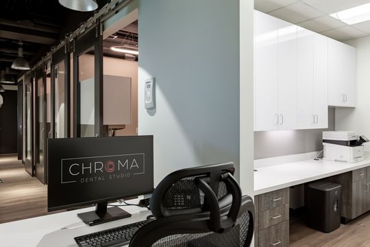 This image of the branded monitor and hallway view at Chroma Dental Studio shows a Chroma monitor, treatment room corridor, frosted glass partitions, and clinical equipment.