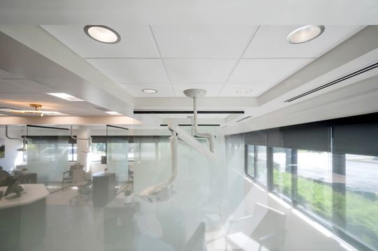 A bright treatment bay at Foundations Orthodontics with glass partitions, overhead clinical equipment, recessed lighting, and large windows.
