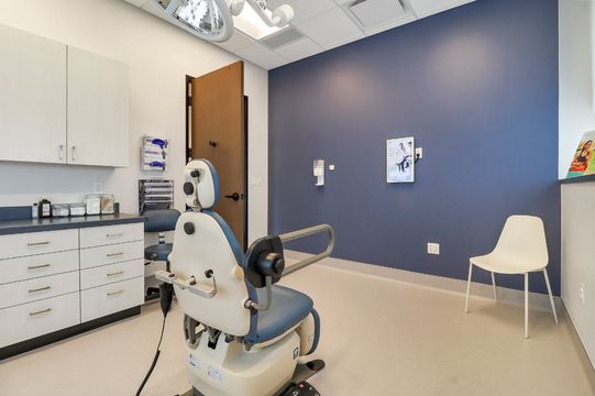 A dermatology exam room at Elevation Dermatology with clinical cabinetry, exam chair, navy accent wall, and patient seating.