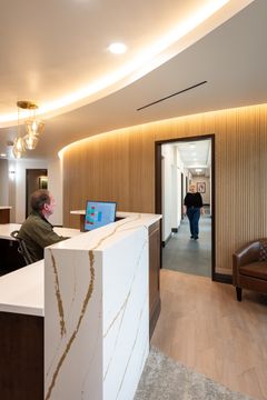 This image of the reception corridor view at Collective Health shows a white reception counter, curved wood feature wall, pendant lighting, and entry hallway access.