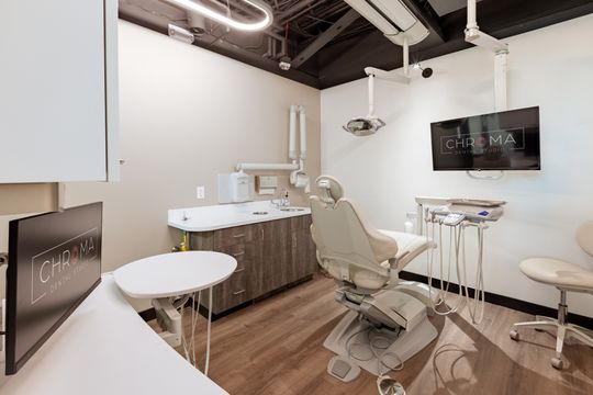 This image of the modern dental operatory at Chroma Dental Studio shows dental chairs, round work surfaces, wall monitors, curved cabinetry, and clean white clinical finishes.
