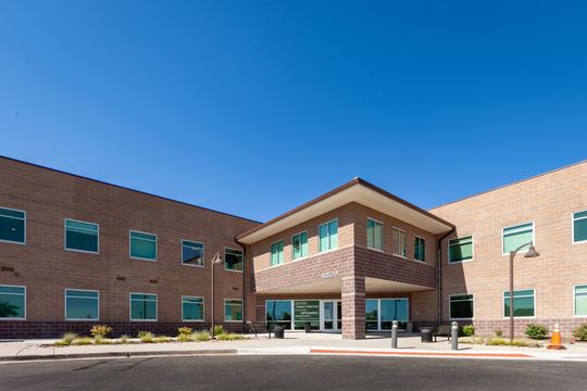 This image of the exterior building at Chroma Dental Studio shows a brick office building, covered entry, large windows, landscaping, and clear blue sky.