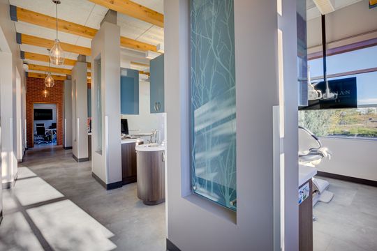 This image of the glass panel hallway detail at Meridian Periodontics of Central Park shows frosted glass panels, treatment room access, wood beams, and clinical hallway circulation.