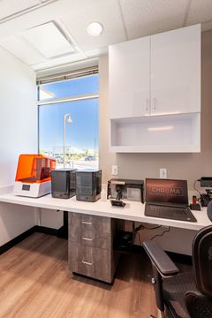 This image of the compact office work area at Chroma Dental Studio shows a workstation, overhead cabinetry, desk chair, window light, and clinical office equipment.