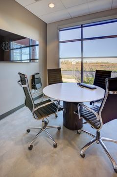 This image of the private consultation table at Meridian Periodontics of Central Park shows a round meeting table, chairs, large window, wall monitor, and compact consultation layout.