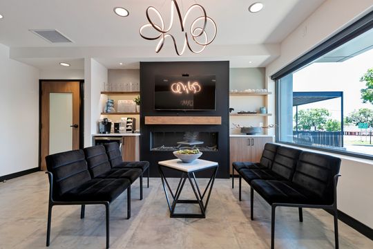 A comfortable waiting room at Arvada Dental Center with black upholstered seating, a fireplace feature wall, large front window, decorative shelving, and a sculptural modern chandelier.
