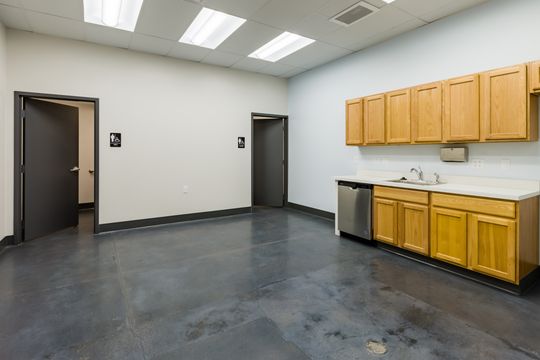 This image of the utility room with yellow cabinets at Montclair Animal Clinic shows yellow wall cabinets, sink counter, dark flooring, doors, and open utility room space.