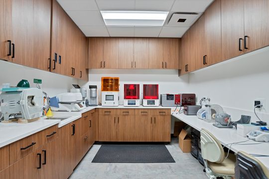 A fully equipped dental lab at Arvada Dental Center with wood cabinetry, digital dental equipment, 3D printing technology, work counters, and organized clinical production space.