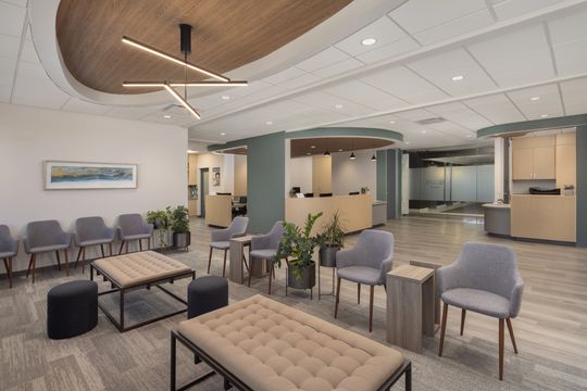 This image of the waiting lounge at Core Dermatology shows lounge chairs, upholstered bench seating, side tables, plants, and a modern dermatology reception area.