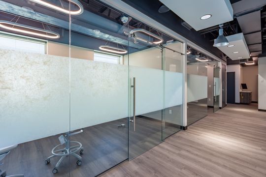 This image of the frosted glass corridor at Chroma Dental Studio shows glass partitions, frosted panels, wood flooring, treatment room openings, and exposed ceiling detail.