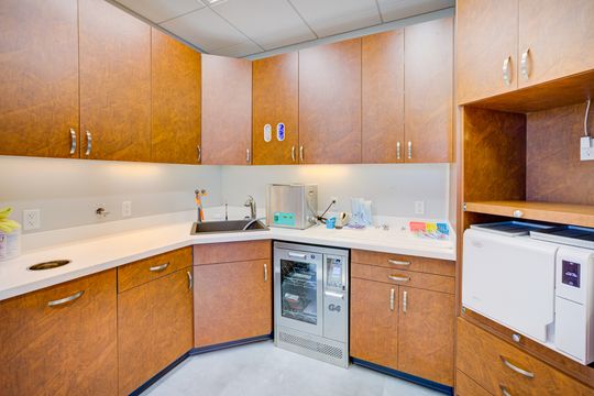This image of the clinical lab work area at Meridian Periodontics of Central Park shows wood cabinetry, sink station, white countertops, dental equipment, and bright task lighting.
