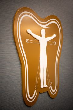 This image of the illuminated tooth logo wall at Collective Health shows a glowing tooth-shaped logo sign, neutral wall texture, and warm accent lighting.