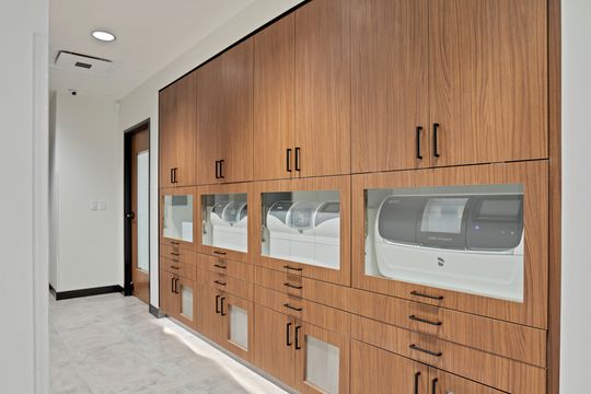 A technology-focused view at Arvada Dental Center showing integrated digital dentistry equipment housed within custom wood cabinetry, including CEREC milling systems and organized storage.