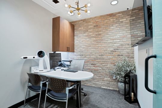 A private consultation room at Arvada Dental Center with a brick feature wall, modern desk, patient seating, computer workstation, wood cabinetry, decorative lighting, and a warm professional atmosphere.