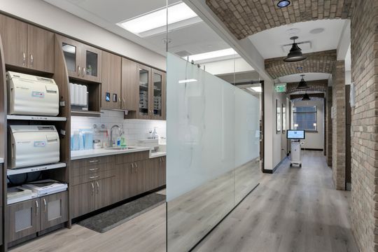 This image of the sterilization corridor at Soult and Swanson Family Dentistry shows countertop equipment, brown cabinetry, frosted glass partition, brick archway, and long hallway view.