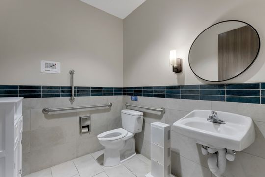 This image of the accessible restroom detail at Soult and Swanson Family Dentistry shows toilet, sink, round mirror, grab bars, blue tile band, and clean patient restroom finishes.