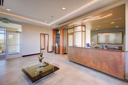 This image of the wide reception lobby at Meridian Periodontics of Central Park shows a spacious waiting area, reception counter, purple sofa, coffee table, and large windows.