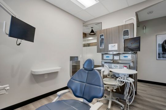This image of the dental operatory equipment view at Soult and Swanson Family Dentistry shows a blue dental chair, wall monitor, instrument trays, sink, and modern clinical equipment.