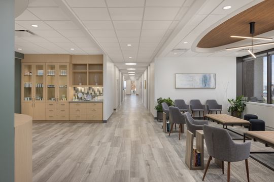 This image of the waiting hall with display cabinets at Core Dermatology shows patient seating, product display cabinetry, wood ceiling accents, and a long clinical corridor.