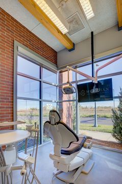 This image of the operatory with window view at Meridian Periodontics of Central Park shows a dental chair, wall monitor, brick wall, round work counter, and floor-to-ceiling window light.