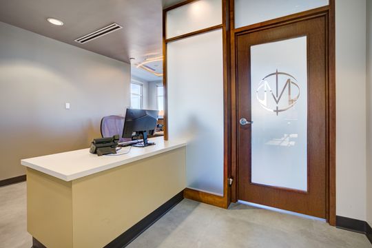 This image of the reception check-in counter at Meridian Periodontics of Central Park shows a reception counter, glass door, frosted branding, computer monitor, and wood trim details.