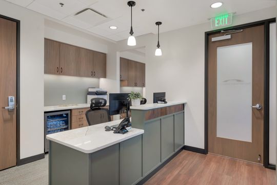 A welcoming reception desk at Bridge Creek Dentistry featuring green cabinetry, wood accents, pendant lighting, computer workstations, and a clean modern front office layout.