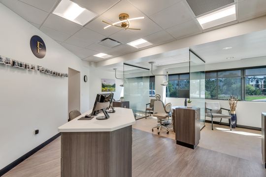 An open treatment area at Foundations Orthodontics featuring glass treatment rooms, modern cabinetry, a clinical workstation, and branded wall details.