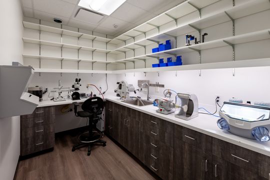 This image of the sterilization workroom at Chroma Dental Studio shows sterilization machines, dark cabinetry, white counters, open shelving, and organized clinical equipment.