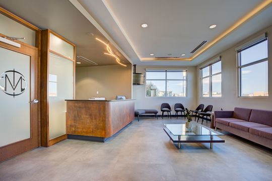This image of the reception lounge view at Meridian Periodontics of Central Park shows purple seating, coffee table, reception counter, large windows, and warm ceiling lights.