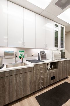 This image of the clinical cabinetry detail at Chroma Dental Studio shows white cabinetry, open glass-front cabinet, countertop workspace, and clean operatory storage.