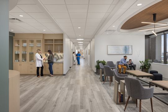 This image of the patient corridor and waiting area at Core Dermatology shows patients and staff, long corridor, waiting chairs, display cabinetry, and warm wood ceiling detail.