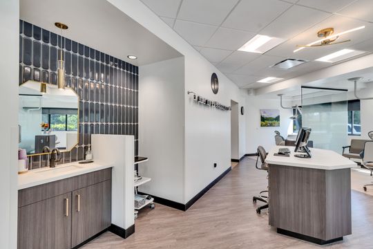 A wide view of the Foundations Orthodontics clinical workspace with dark tile, brass accents, glass treatment rooms, and modern cabinetry.