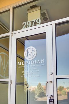 This image of the glass entry door detail at Meridian Periodontics of Central Park shows branded glass door, street number, exterior reflections, and metal door framing.