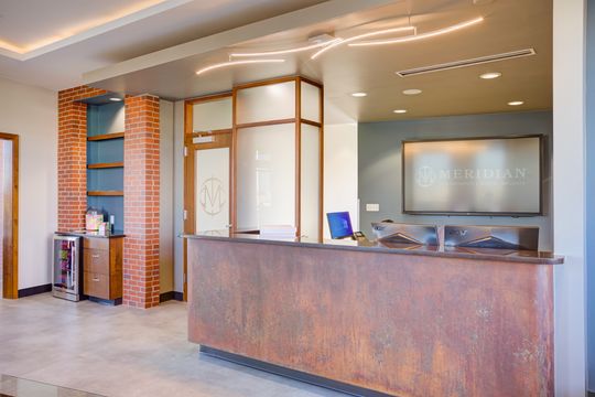 This image of the reception counter detail at Meridian Periodontics of Central Park shows a stone front desk, brick accent wall, wood trim, computer monitor, and warm lighting.