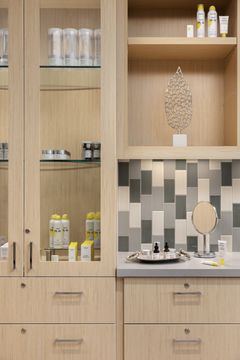 This image of the product display cabinet at Core Dermatology shows open shelving, skincare products, wood cabinetry, tile backsplash, and decorative display items.