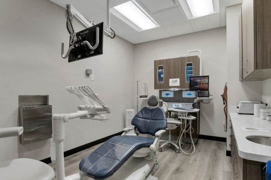 This image of the dental treatment room at Soult and Swanson Family Dentistry shows a blue dental chair, wall monitor, dental tools, sink, and compact operatory cabinetry.
