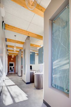 This image of the operatory hallway at Meridian Periodontics of Central Park shows treatment room openings, wood ceiling beams, glass partitions, and bright corridor lighting.