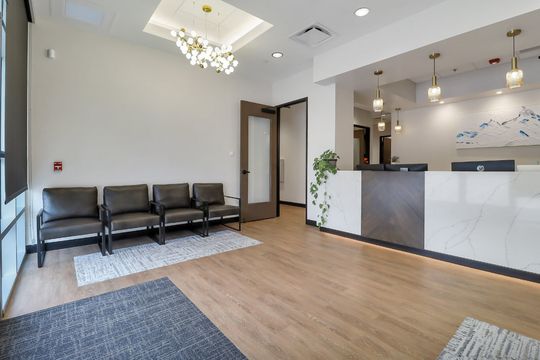 The Elevation Dermatology reception area with modern front desk, comfortable seating, warm wood flooring, and decorative lighting.