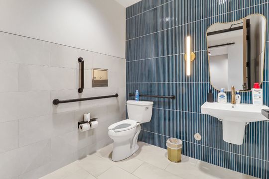 An accessible restroom at Elevation Dermatology featuring blue tile, grab bars, wall-mounted sink, mirror, and modern fixtures.