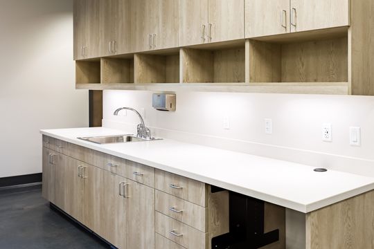 This image of the prep counter and open shelving at Montclair Animal Clinic shows a long white counter, open cubby shelving, sink, light wood cabinetry, and clean work surface.